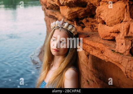 Giovane donna in corona da conchiglie che si trovano vicino al muro di sabbia rossa vicino al fiume Foto Stock