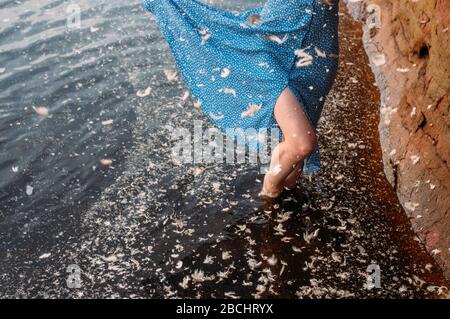 Ragazza che rimane in acqua vicino al muro di sabbia rossa nel fiume, molte piume in acqua Foto Stock