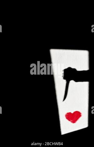 l'ombra di una mano con un coltello è proiettata su una parete bianca con un cuore rosso Foto Stock