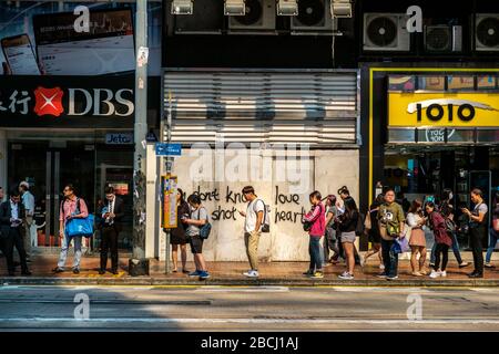 Hong Kong - Novembre 2019: Persone in coda per strada, in attesa di un autobus che cerca un telefono cellulare a Hong Kong Foto Stock