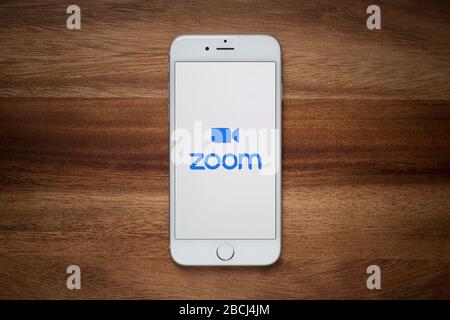 Un iPhone che mostra il sito di videoconferenza Zoom si appoggia su una semplice tabella di legno (solo per uso editoriale). Foto Stock