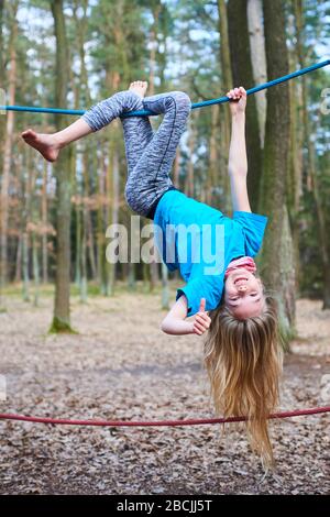 Ragazza giovane bambino appeso sulla corda capovolta sul parco giochi nel parco Foto Stock