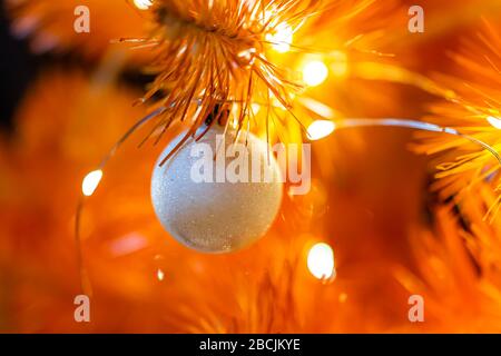 Macro closeup di colorful giallo dorato decorazione lucido ornamento appeso su albero di Natale di Capodanno con illuminazioni luminose in inverno a Lviv, Ukrai Foto Stock