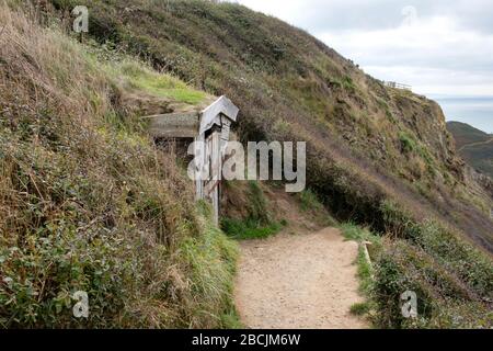 Il cartello in pietra del National Trust è chiaramente visibile dal South West Coast Path e segna il sentiero verso il basso fino al rifugio di Hawker Foto Stock