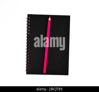 Matita rosa sulla parte superiore di un diario di carta di singola nota coperto di colore nero isolato su uno sfondo bianco vuoto Foto Stock