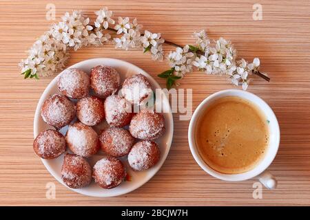 La mattina inizia con un caffè e ciambelle fatte in casa con un brach fiorente sulla scrivania, durante l'isolamento pandemico Foto Stock