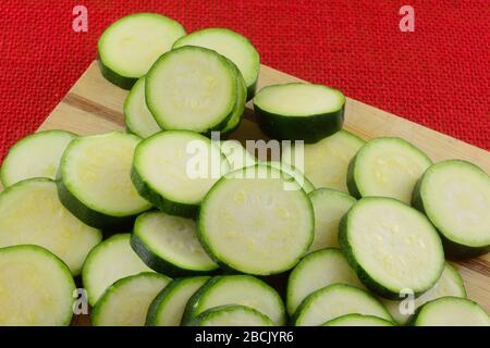 Zucchine fresche e crude a fette su tagliere di legno su tavolo rosso Foto Stock