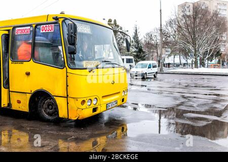 Rivne, Ucraina - 28 dicembre 2019: Autobus giallo alla fermata con bagnati pudle su asfalto in Ucraina Rovno città in stazione ferroviaria in inverno Foto Stock