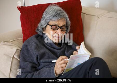 Persona anziana che legge un libro di puzzle, schermando o auto-isolando durante il blocco di scoppio di coronavirus nel Regno Unito Foto Stock