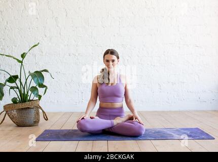 Giovane attraente donna yoga praticare yoga, allenarsi, indossare abbigliamento sportivo viola, stile urbano fresco, a tutta lunghezza, studio bianco Foto Stock