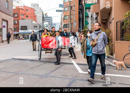 Tokyo, Giappone - 30 marzo 2019: Area di Asakusa nel centro della città in una giornata torbida con traffico su strada e turisti in sella a una guida turistica in risciò Foto Stock