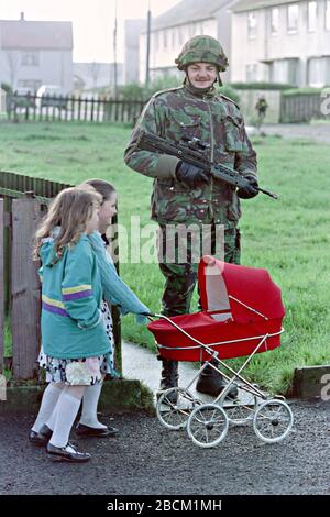 Giovani ragazze irlandesi spingono un pram di bambole oltre un soldato britannico che pattugliano l'area di Bogside 25 gennaio 1992 a Londonderry, Irlanda del Nord. Le forze di sicurezza hanno intensificato i pattugliamenti e le ricerche nella zona prima del 20th anniversario del massacro di Bloody Sunday. Foto Stock