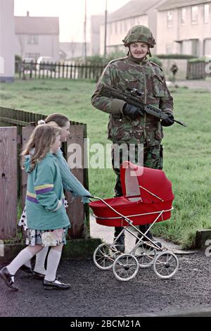 Giovani ragazze irlandesi spingono un pram di bambole oltre un soldato britannico che pattugliano l'area di Bogside 25 gennaio 1992 a Londonderry, Irlanda del Nord. Le forze di sicurezza hanno intensificato i pattugliamenti e le ricerche nella zona prima del 20th anniversario del massacro di Bloody Sunday. Foto Stock