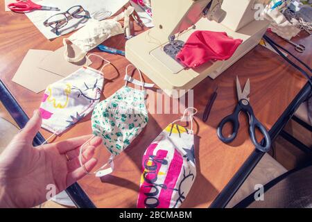 Una pila di maschere cucite in tessuto con motivi colorati. La gente sta facendo maschere per coprire la mancanza di forniture di DPI per gli ospedali. Foto Stock