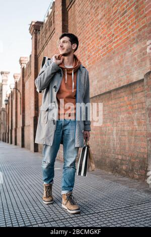 Ritratto di giovane bell'uomo che tiene borse per lo shopping mentre cammina sulla strada. Urbano, concetto di negozio. Foto Stock