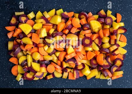 Pila di carote a dadini arcobaleno su un tagliere nero, come sfondo Foto Stock