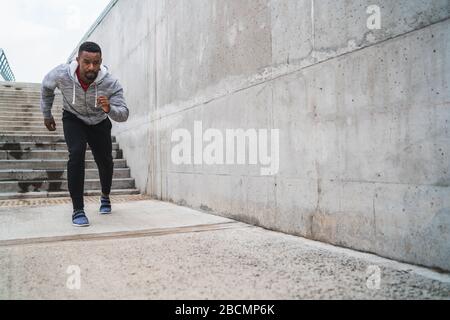 Ritratto di un uomo atletico che corre sulla strada su sfondo grigio. Sport e stile di vita sano. Foto Stock