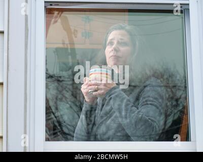 Oak Park, Illinois, Stati Uniti. 4th aprile 2020. Una donna guarda fuori la sua finestra di cucina durante COVID-19 shelter-in-Place ordine. Essere bloccati a casa può portare sentimenti di isolamento e solitudine. Foto Stock