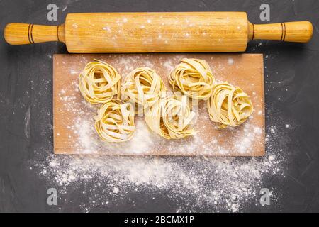 Varietà di spaghetti e tagliatelle di pasta cruda, fatti in casa, con farina su tavola di legno a dondolo per la pasta su pasta nera Foto Stock