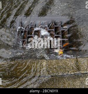 La pioggia intensa ha causato l'inondazione nella strada, l'acqua che vorticava intorno allo scarico della tempesta Foto Stock