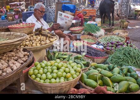 Un venditore di frutta e verdura nel mercato di Bhuleshwar, Mumbai, India, siede circondato dai suoi articoli leggendo il giornale di lingua marathi Nava Kaal (Nuova era) Foto Stock