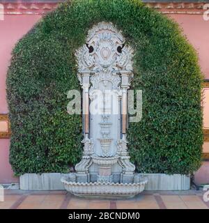 Fontana con pareti scolpite in marmo bianco circondata da foglie verdi su pareti in pietra rosa e pavimento in ceramica arancione piastrellato in piazza Sultan Ahmed, Istanbul, Turchia Foto Stock