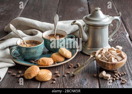 Due tazze vintage blu di caffè nero, biscotti e una caffettiera di peltro antica circondata da tovaglioli di lino grigio, pezzi di zucchero e chicchi di caffè sulla vecchia volontà Foto Stock