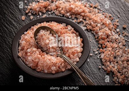 Sale rosa Himalayan in ciotola e cucchiaio su fondo nero Foto Stock