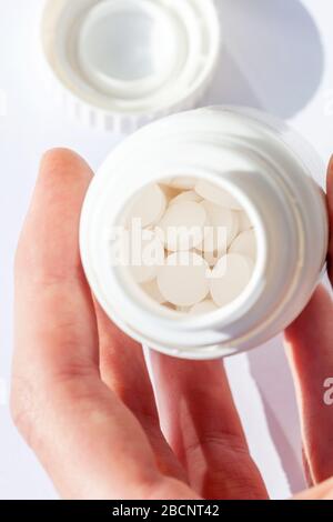 Uomo che guarda in un piccolo contenitore aperto per pillole con pillole bianche all'interno in un ambiente sterile, tenendolo in mano, esaminandolo. Assunzione di farmaci Foto Stock