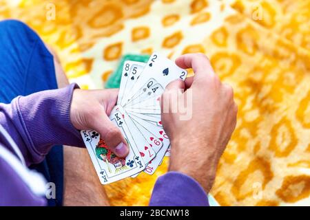 Giovane uomo in abbigliamento casual che gioca carte seduti su un blaket fuori, mani primo piano, la raccolta di una carta due di picche, tenendo un mazzo completo sparso fuori Foto Stock