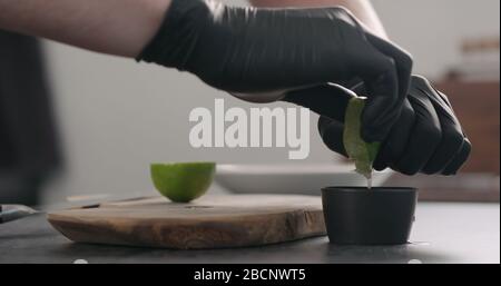 mani dell'uomo in guanti neri schiacciare il lime in una ciotola nera Foto Stock