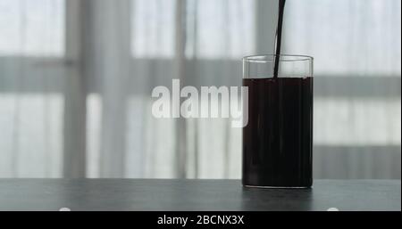 versare il succo di mirtillo nell'acqua in vetro sul piano di cemento con finestra sullo sfondo Foto Stock