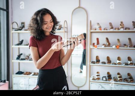 donna asiatica shopping scarpe in boutique. cliente che guarda il prezzo del prodotto Foto Stock