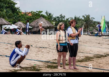 Turisti sulla spiaggia in attesa di un giro in aquilone, Bali, Indonesia Foto Stock