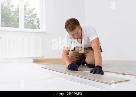 Installazione laminato o parquet in camera, lavoratore installazione in legno pavimenti in laminato, segnando la lunghezza del laminato Foto Stock