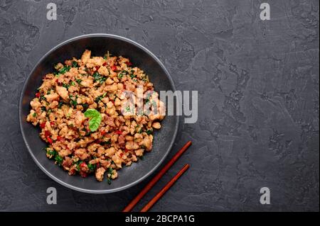 Pad Krapow Gai - pollo al basilico tailandese in ciotola nera su sfondo di ardesia scuro. Pad Krapow è un piatto di cucina tailandese con carne di pollo o maiale tritata, basilico, s. Foto Stock