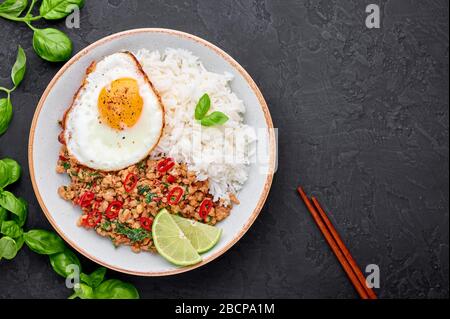 Pad Krapow Gai - pollo al basilico tailandese con riso e uovo fritto sfondo nero ardesia. Pad Krapow è un piatto di cucina tailandese con pollo tritato o carne di maiale, Foto Stock