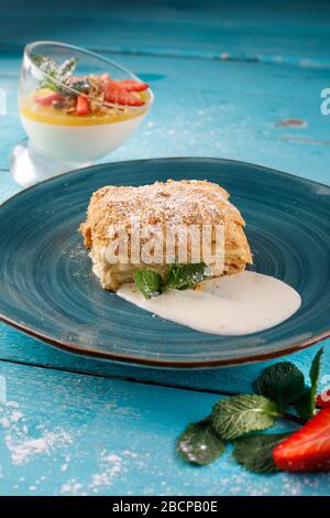 Strato torta con crema Napoleone milfey vaniglia fetta con menta su uno sfondo blu piatto Foto Stock