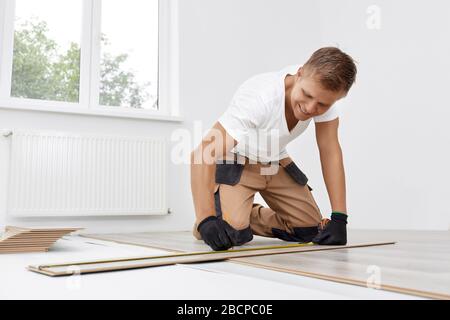 Artigiano professionista mette laminato in un nuovo appartamento. Il falegname misura la linea di taglio sul laminato. Riparazione del pianale in legno. Foto Stock