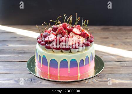 Torta di colore rosa e blu con cioccolato bianco fuso con ciliegie fresche, lamponi e fragole. Rustico sfondo in legno. Foto Stock