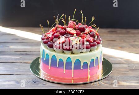 Torta di colore rosa e blu con cioccolato bianco fuso con ciliegie fresche, lamponi e fragole. Rustico sfondo in legno. Foto Stock