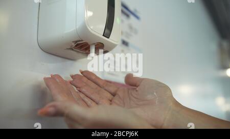 Primo piano lavando le mani con un dispenser automatico di igienizzante per alcol in aeroporto. Mano donna per gel di alcol sotto igienizzatore automatico. Foto Stock
