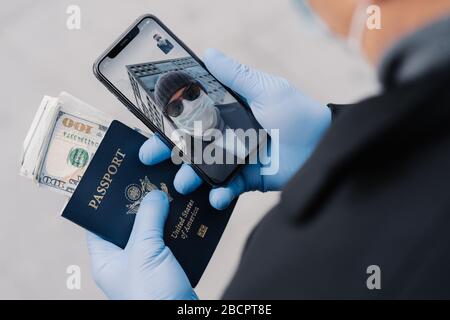 L'uomo irriconoscibile ha videochiamata, parla con l'amico, indossa guanti di gomma medica di protezione, tiene il passaporto con soldi, andando lasciare il paese durante Foto Stock