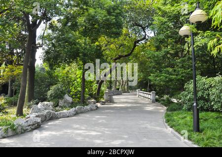 Un percorso concreto attraverso un parco nella concessione francese a Shanghai, Cina. Il sentiero è circondato da alberi e lanterne e conduce ad un piccolo bra bianco Foto Stock