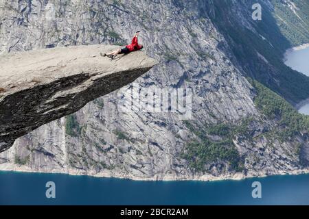 L'uomo adulto si trova sulla formazione rocciosa di Trolltunga e fa selfie con lo smartphone. La scogliera è a Odda, nella contea di Hordaland, Norvegia, Europa Foto Stock