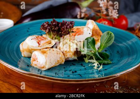 Pancake con salmone e verde su uno sfondo di piatti blu sullo sfondo di tavolo in legno. Foto Stock