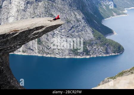 Uomo adulto sdraiato sulla scogliera di Trolltunga sulla schiena. Scattare foto con lo smartphone. Norvegia, Scandinavia Foto Stock