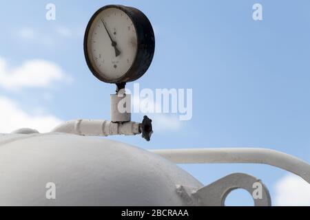 Il manometro industriale rotondo montato su un serbatoio di gas bianco è sotto il cielo blu Foto Stock