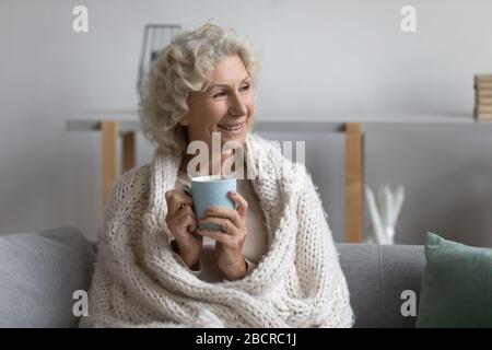 Coperto in maglia calda plaid felice donna senior bere caffè. Foto Stock