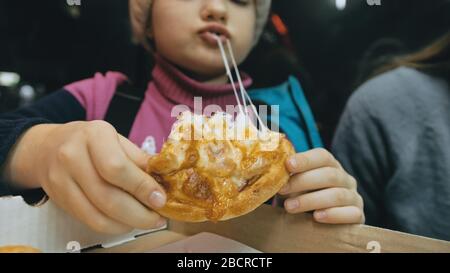 Bambino mangiare pizza formaggio quattro. Primo piano di ragazza giovane donna mangiare pizza e masticare in ristorante all'aperto. Bambini mani prendere pezzo pizza. Foto Stock